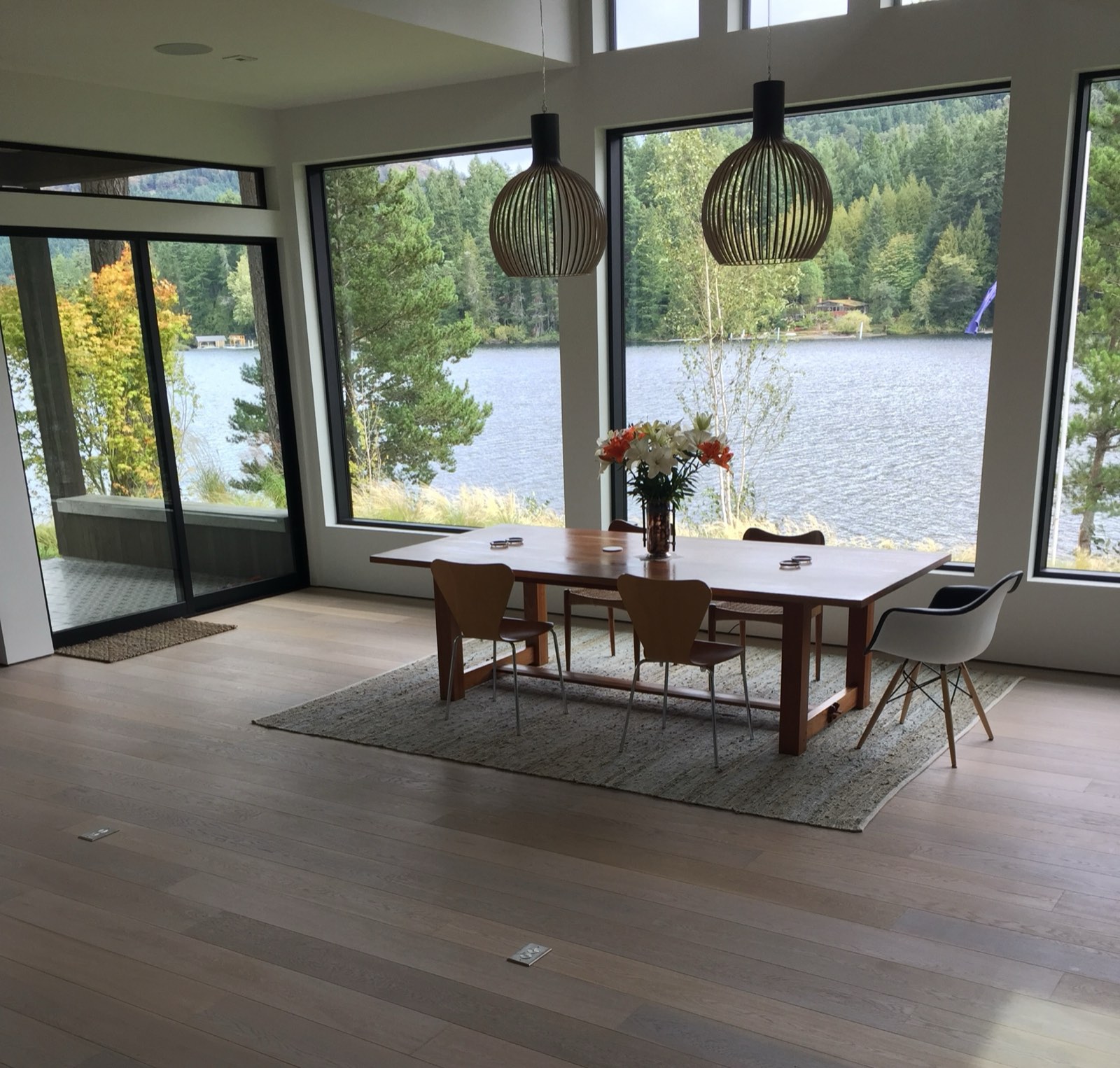 Lakefront dining room with pale wide-plank flooring and floor-to-ceiling windows